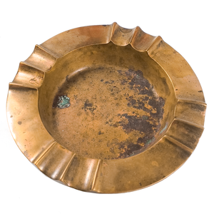 A round brass ash tray with four areas of fluting around the edge, showing a fair amount of patina and some verdigris on the inside