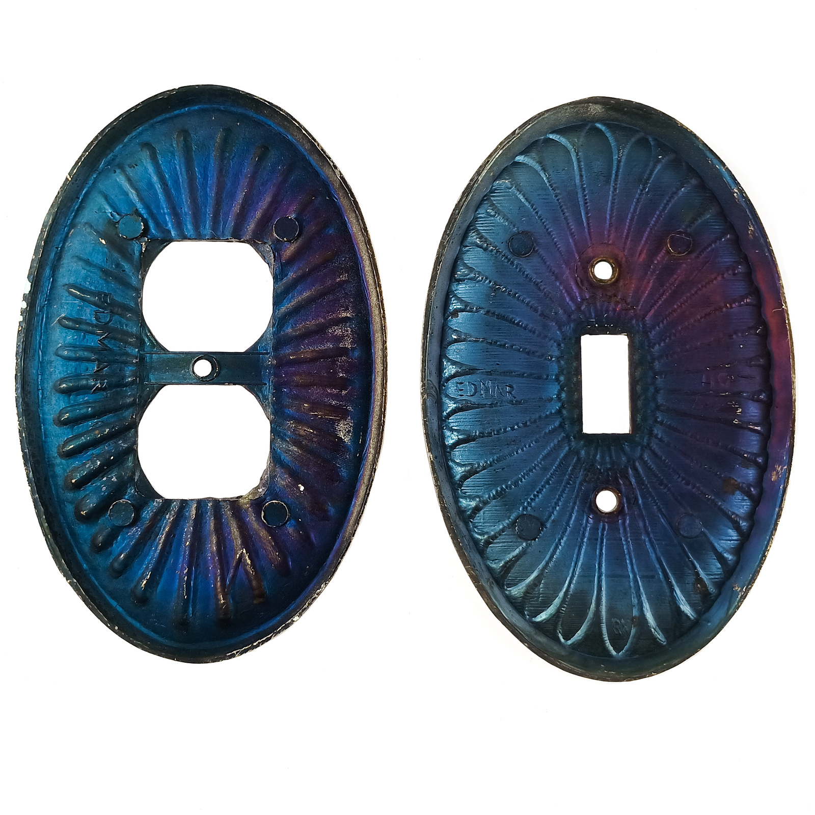 A pair of brass oval electrical plates, each with a design resembling flower petals emerging from the center and dark patina between each petal