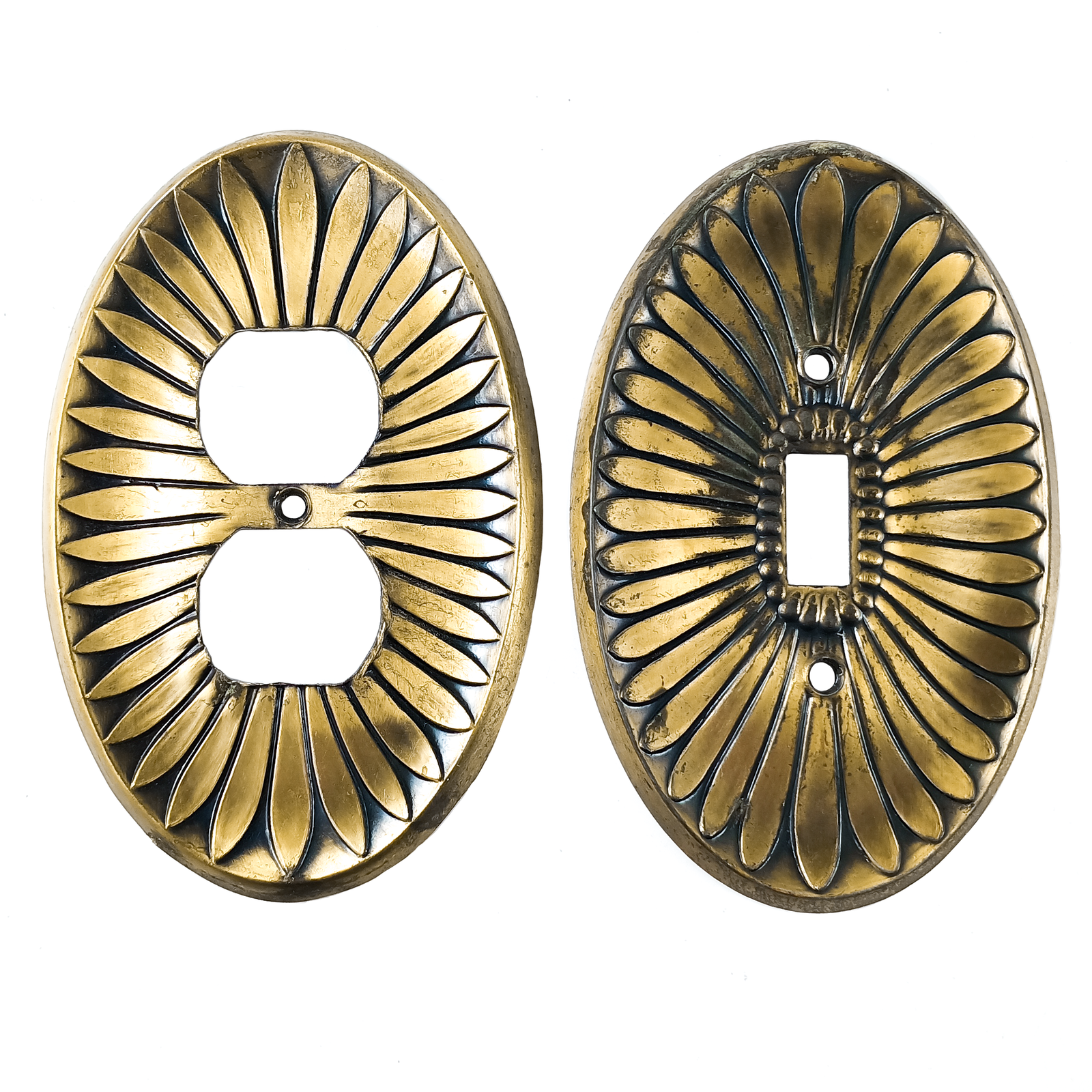 A pair of brass oval electrical plates, each with a design resembling flower petals emerging from the center and dark patina between each petal