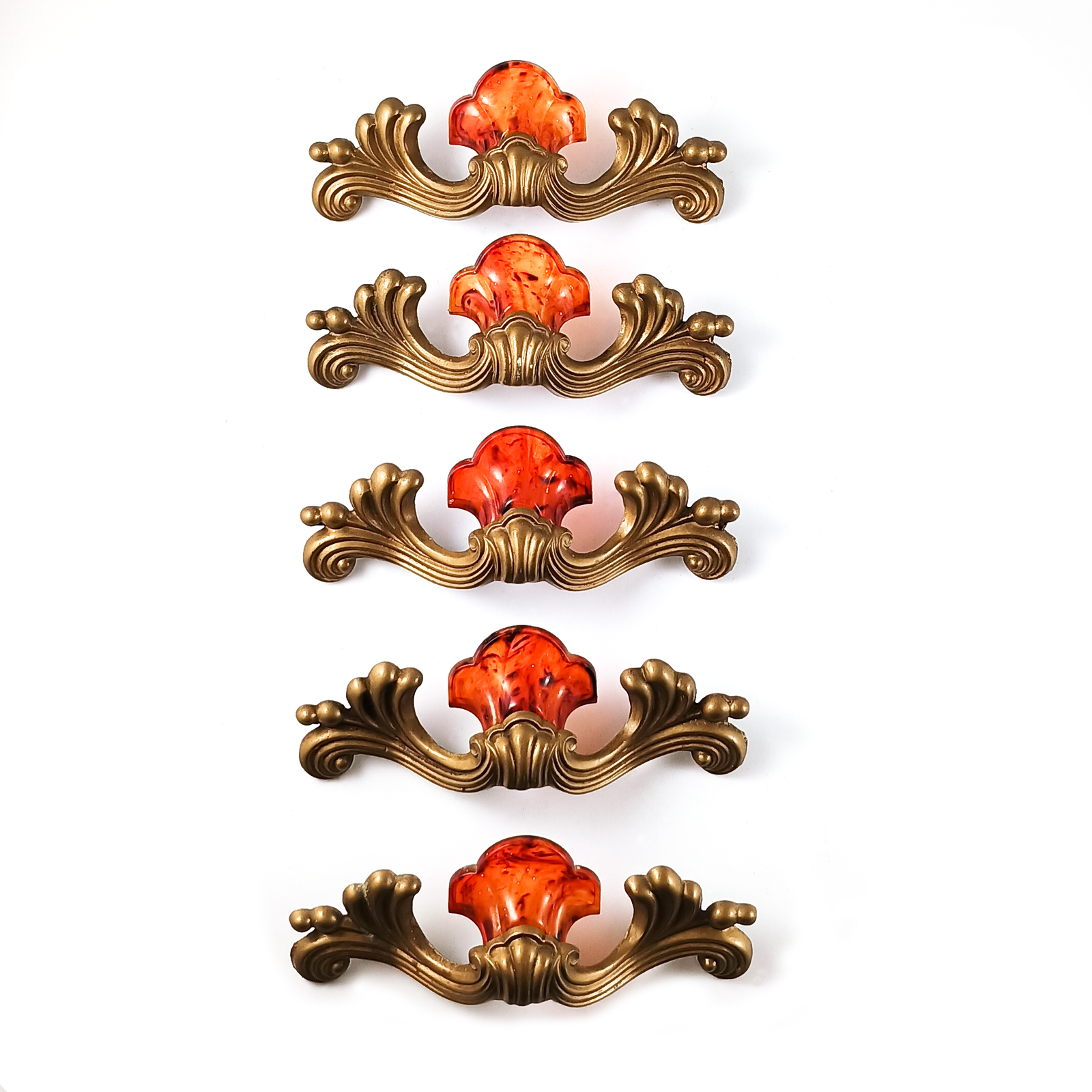 A single drawer handle, primarily gold-tone scrollwork with a shell shape made of marbled orange plastic on the top.