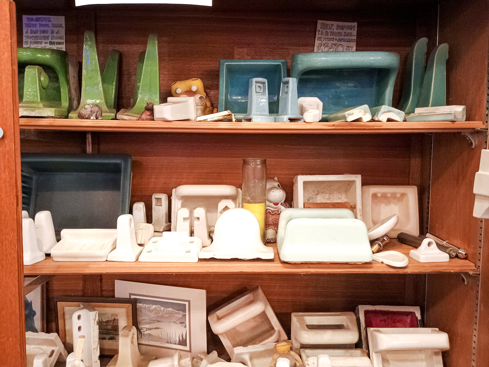 Three shelves of tile-in ceramic bathroom accessories in varying shades of white, blue, and green. Various hippos and tchotchkes are mised in as well.