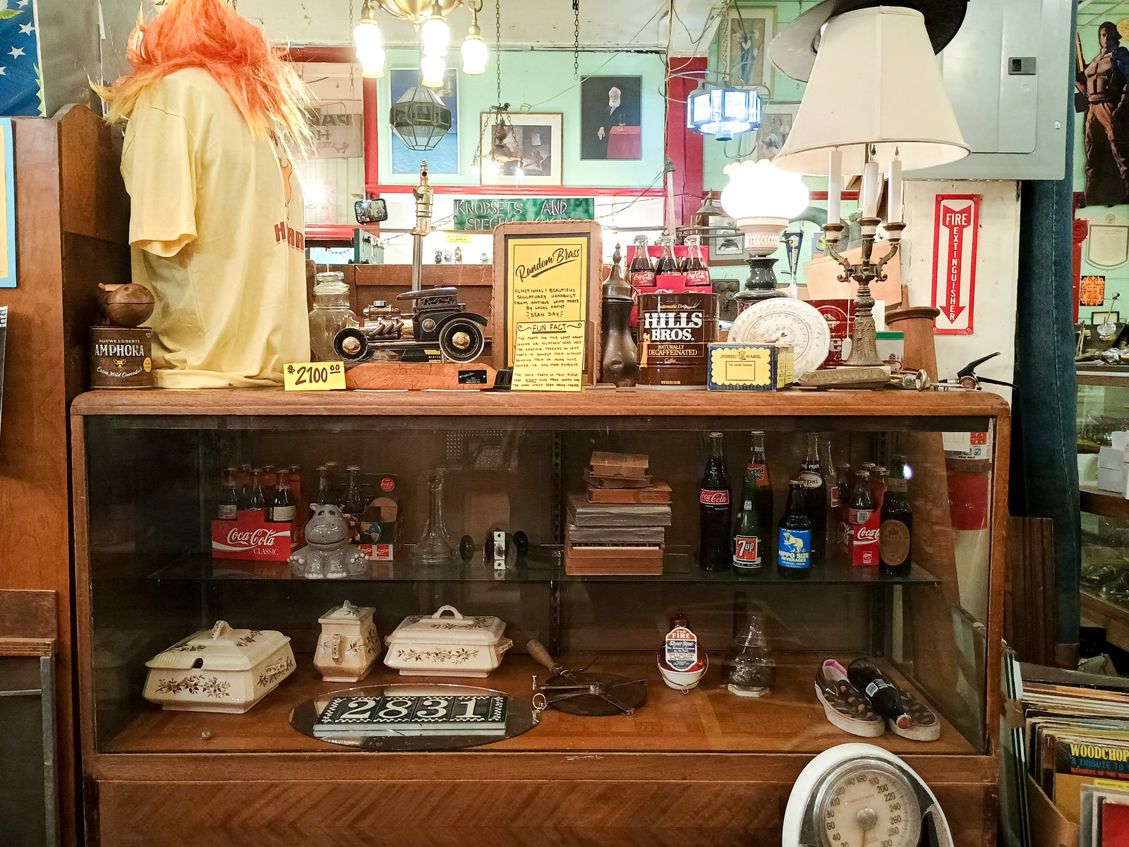 A photo of a glass case. Inside and on top of the case are items such as vintage sodas, ceramic cookware, and a lamp.