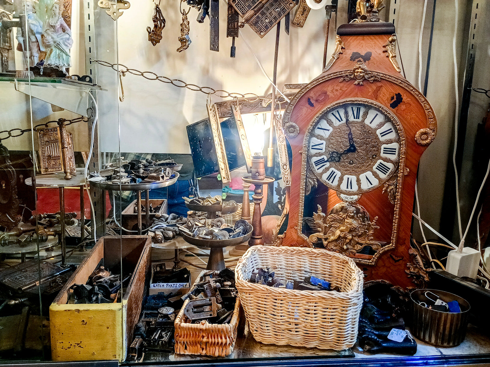 A shelf inside a glass cabinet with any small pieces of antique hardware, as well as a vintage-styled clock