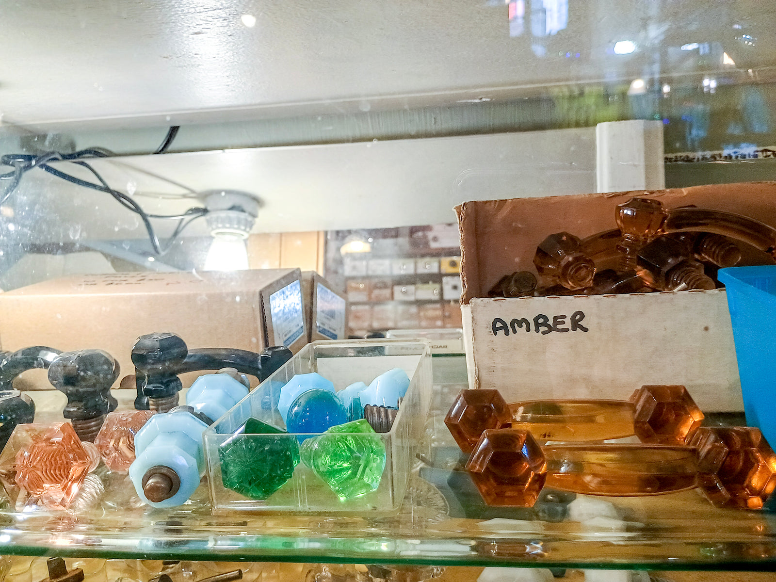 A shelf inside a glass cabinet, covered in colorful glass drawer knobs and handles