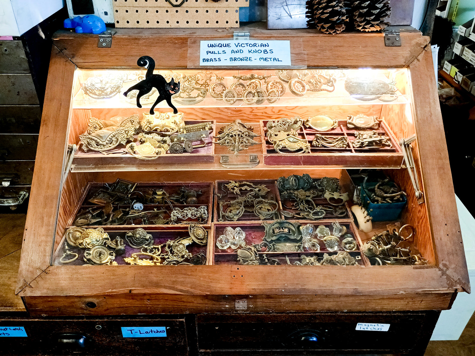 A glass case labeled "Unique Victorian pulls and knobs - brass - bronze - metal." The case is full of drawer handles.