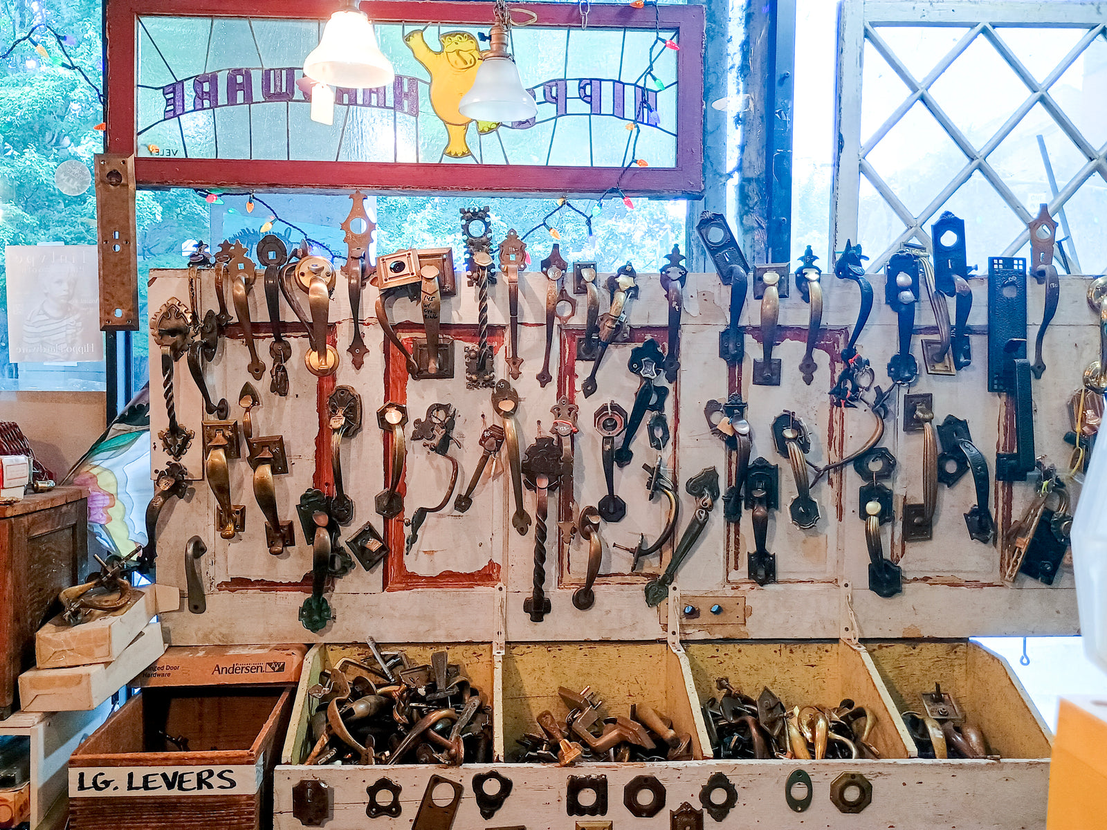 A collection of door handles in front of a stained glass window reading "HIPPO HARDWARE"