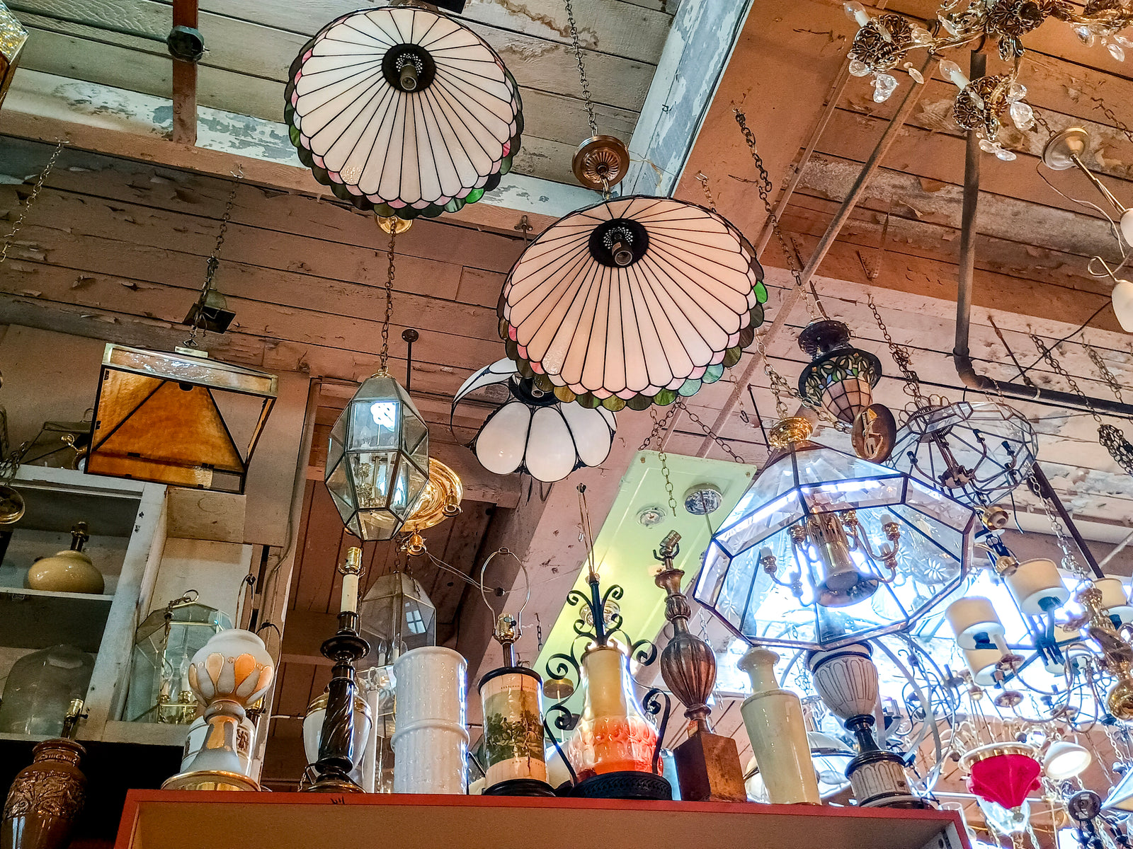 Several lamps and chandeliers hanging from the ceiling, including two matching floral stained glass lamps and several geometric lamps.