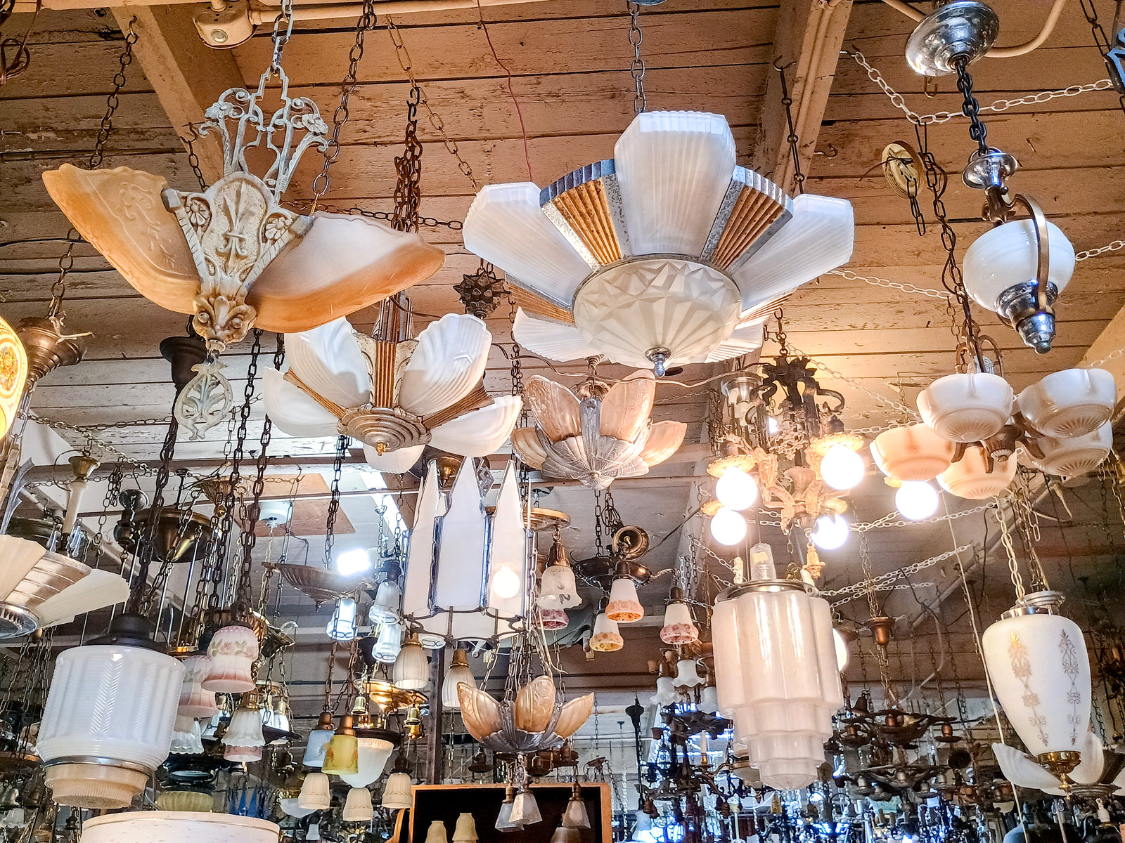 A photo of several chandeliers hanging from a wooden ceiling. Many of the chandeliers have art deco slip shades.