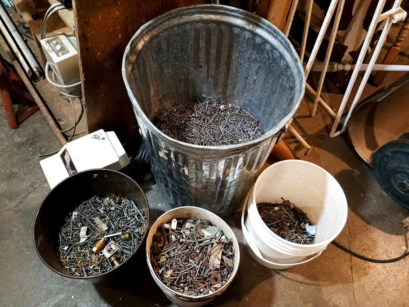 Three buckets and a large metal trash can, all partially filled with nailed, screws, and other various bits of metal hardware.