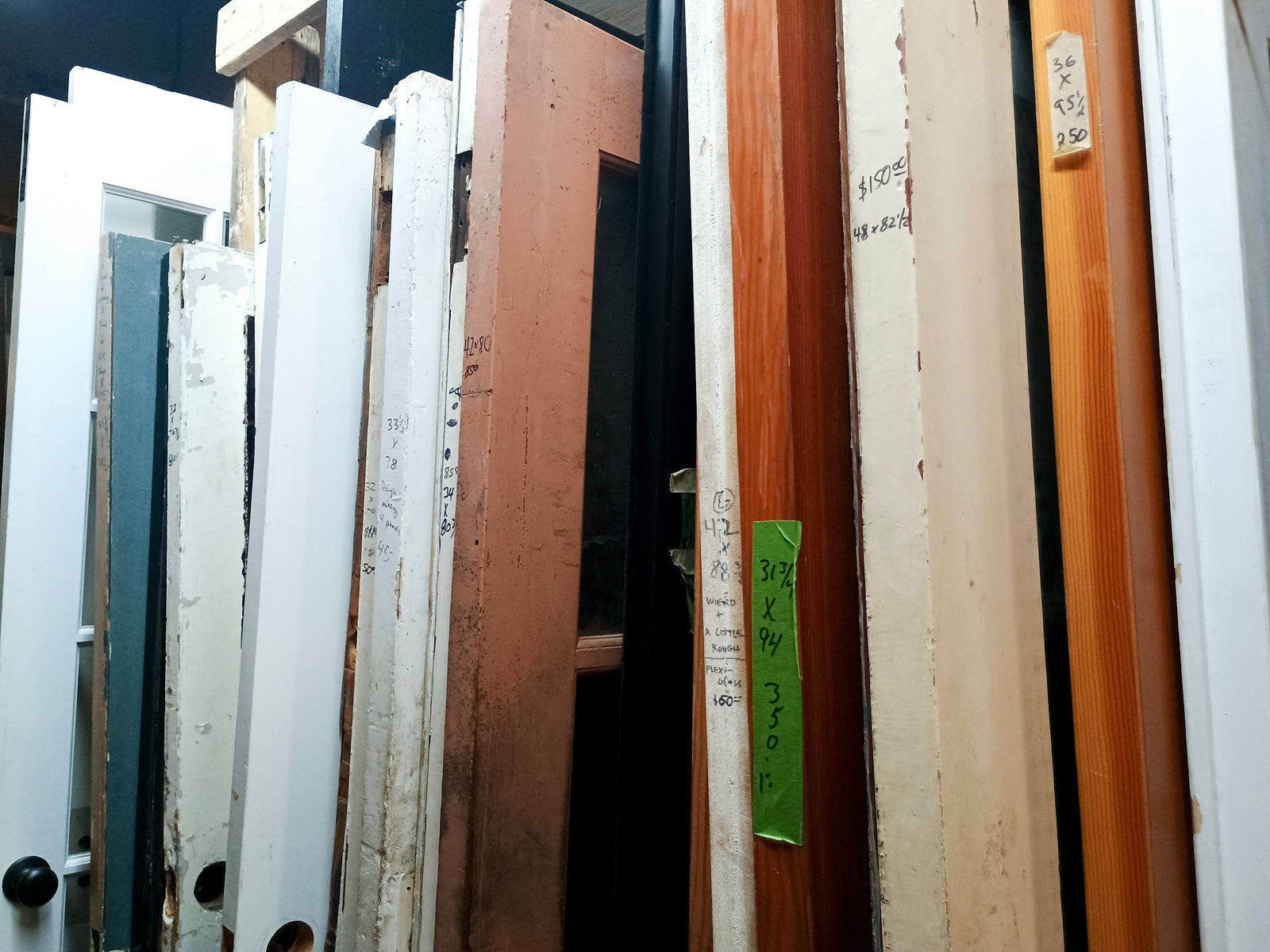 The edges of several doors of varying colors, many of which have prices and sizes written on the side. Prices pictured range from fifty to three hundred and fifty dollars.