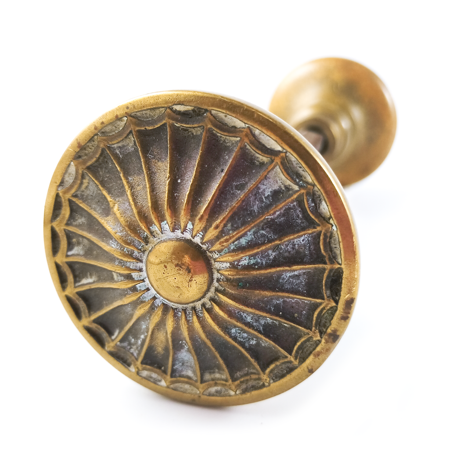 One of the two doorknobs - they have a radial pattern resembling a sunburst, a flower, or a spiderweb around a central round "button," with patina emphasizing the pattern. This knob is a dark, orange-y shade of brass.