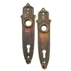 Two bronze escutcheons shaped like saggers with scrolling, somewhat floral decorations