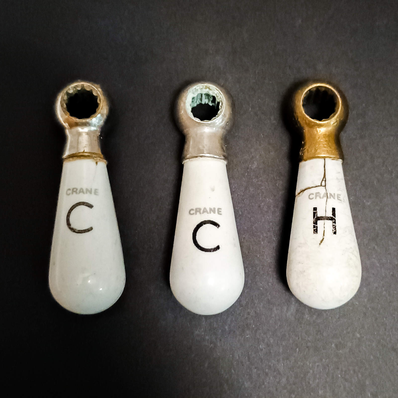 Seven white porcelain teardrop-shaped handles with nickel-plated brass tops, all labeled "CRANE" and either H or C, and in varying conditions