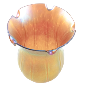 The rim of a golden tulip-shaped lamp shade, showing rainbow iridescence and light shining through a textured surface