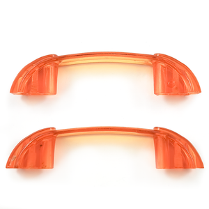 Two bright orange translucent Bakelite drawer handles, with darker orange sections at each end. Yellow patches of light on the background show the way light shines through them.