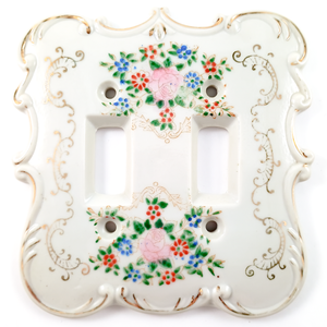 A double-gang light switch plate made of white porcelain, with floral motifs and gilded scrolling designs