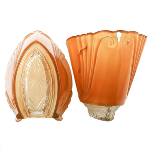 Two glass slip shades with a transparent starburst pattern at the base, along with swirling designs along the sides. One slip shade has a large crack in it and is missing a small bit of its orange coating.