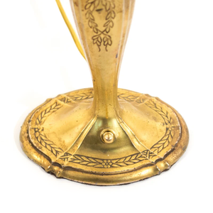 The base of an Art Nouveau brass table lamp shaped like a candlestick, showing the ornate floral detailing