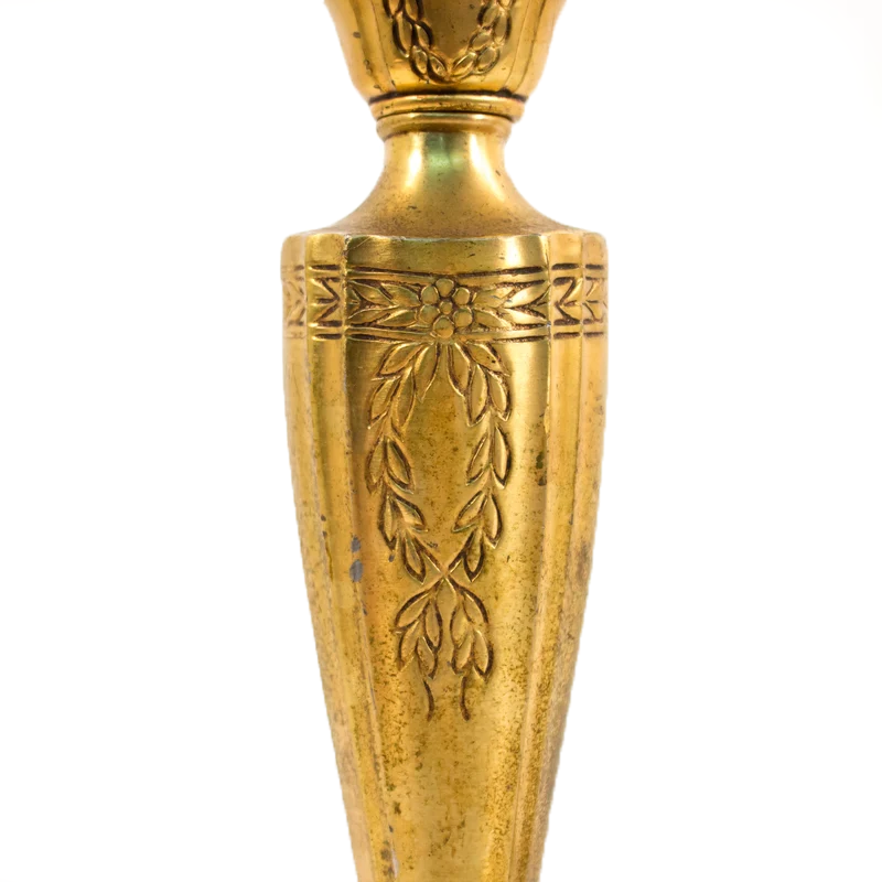 A pair of brass table lamps shaped like candlesticks, complete with faux candles. They have flame-shaped bulbs installed for display, and the brass bases have ornate flower and leaf details.