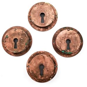 The backs of the four door pulls, showing that the keyhole portions are separate pieces and held in with small brackets. There are small patches of verdigris on some of the door pulls.