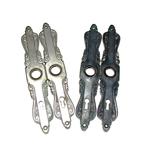 The backs of two sets of Art Nouveau escutcheons, with intricate scrolling details. One set is silver-tone on the back, and the other has been treated to have a black patina finish