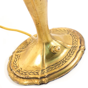The base of an Art Nouveau brass table lamp shaped like a candlestick, showing the ornate floral detailing