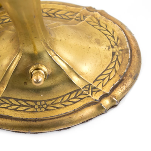 The base of an Art Nouveau brass table lamp shaped like a candlestick, showing the ornate floral detailing