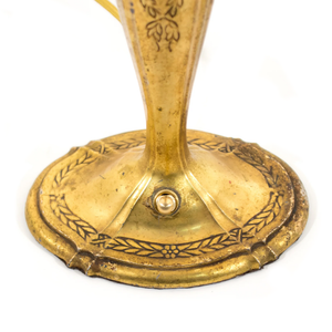 The base of an Art Nouveau brass table lamp shaped like a candlestick, showing the ornate floral detailing