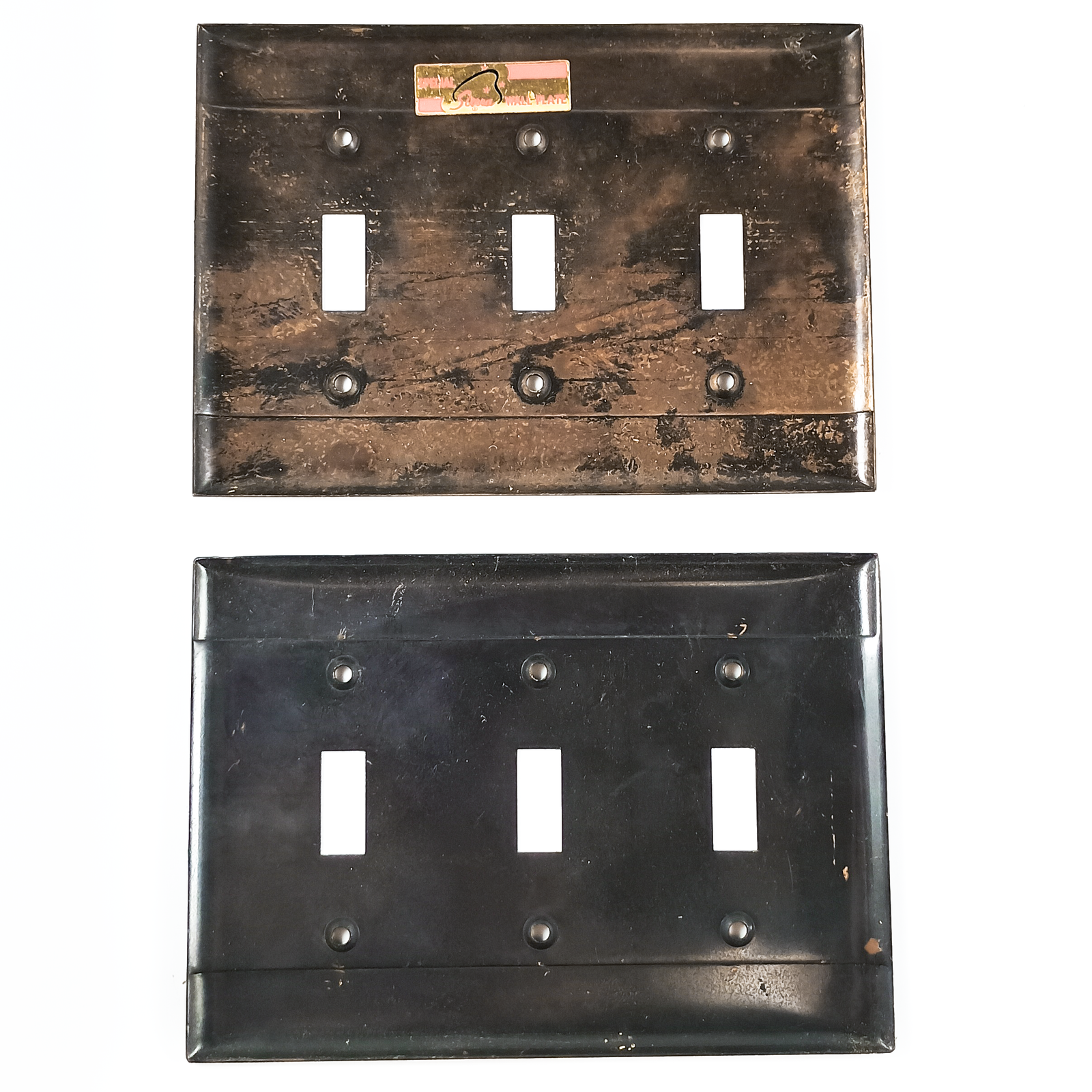 Two light switch plates, each with six screw holes and three openings for switches. One plate is a light bronze, with two very distinct stripes of dark patina going horizontally across the screw holes. The other plate has the same stripes, but is overall darker in finish, and the stripes are blurred at the edges. Both plates have some surface stains or what may be adhesive residue. as well as areas of uneven finish.