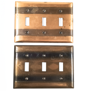 Two light switch plates, each with six screw holes and three openings for switches. One plate is a light bronze, with two very distinct stripes of dark patina going horizontally across the screw holes. The other plate has the same stripes, but is overall darker in finish, and the stripes are blurred at the edges. Both plates have some surface stains or what may be adhesive residue. as well as areas of uneven finish.