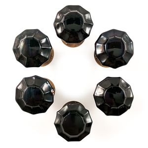 Six black glass knobs arranged in a circle on a white background. The knobs are 10-sided with fluted facets, and each appears to be sitting on a round aged bronze base.