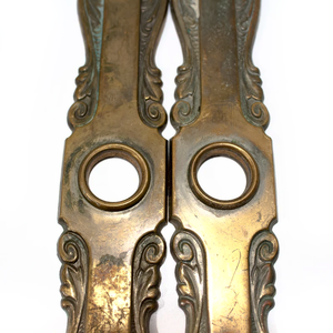 A close-up of two brass Art Nouveau escutcheons, showing the ornate decorations and some surface wear around the doorknob bezels
