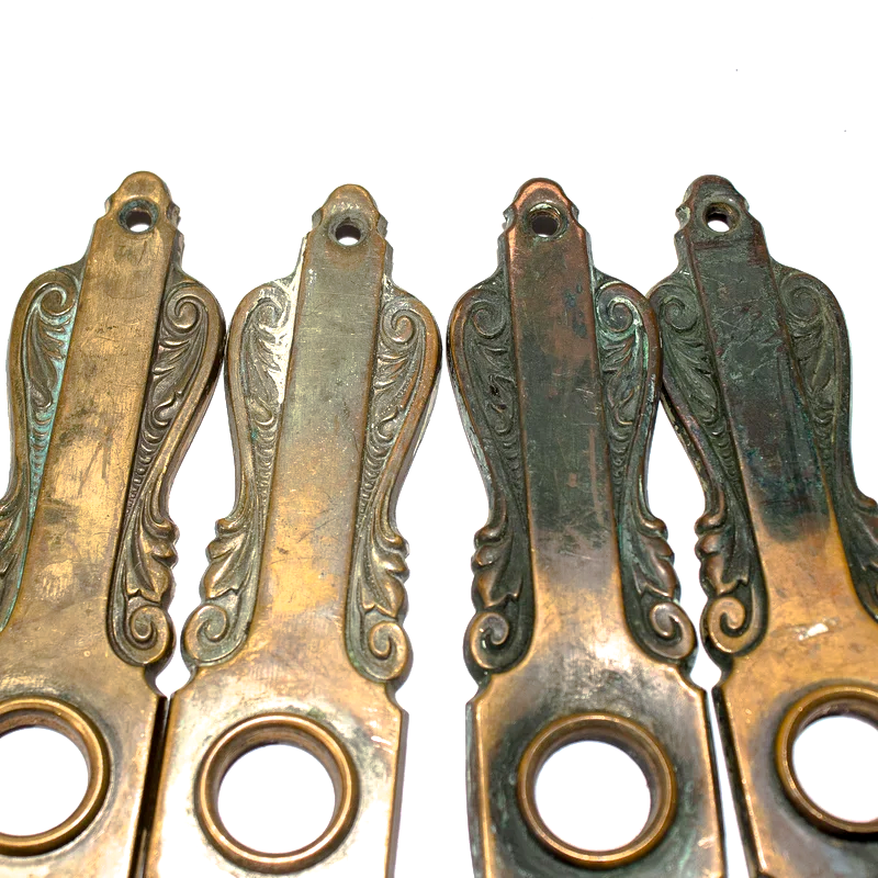 Two sets of Art Nouveau escutcheons, with intricate scrolling details, a central bezel for a doorknob, and keyholes at the bottom. Two of the escutcheons have a lighter brass finish, and two have a dark patina-coated bronze finish.
