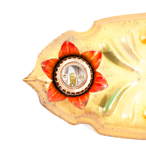 A close-up of a light socket in a vintage gold-tone fixture. The socket is surrounded by metal flower petals which have been painted red.