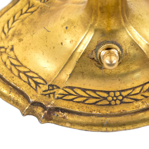 The base of an Art Nouveau brass table lamp shaped like a candlestick, showing the ornate floral detailing