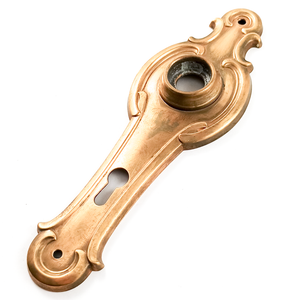 An angled photo of a vintage brass escutcheon, showing that the surface is slightly matte from a previous polishing attempt.