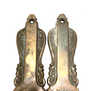 A close-up of the tops of two brass Art Nouveau escutcheons, showing the ornate details