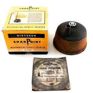 A vintage Dietzgen Sharpoint lead pointer made of cast iron with a cork grip, photographed alongside its graphite-stained original paper insert and its original yellow box