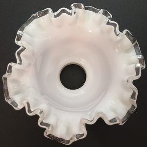 The interior of a ruffled milk glass lamp shade with clear glass along the edges, photographed on a dark grey background.