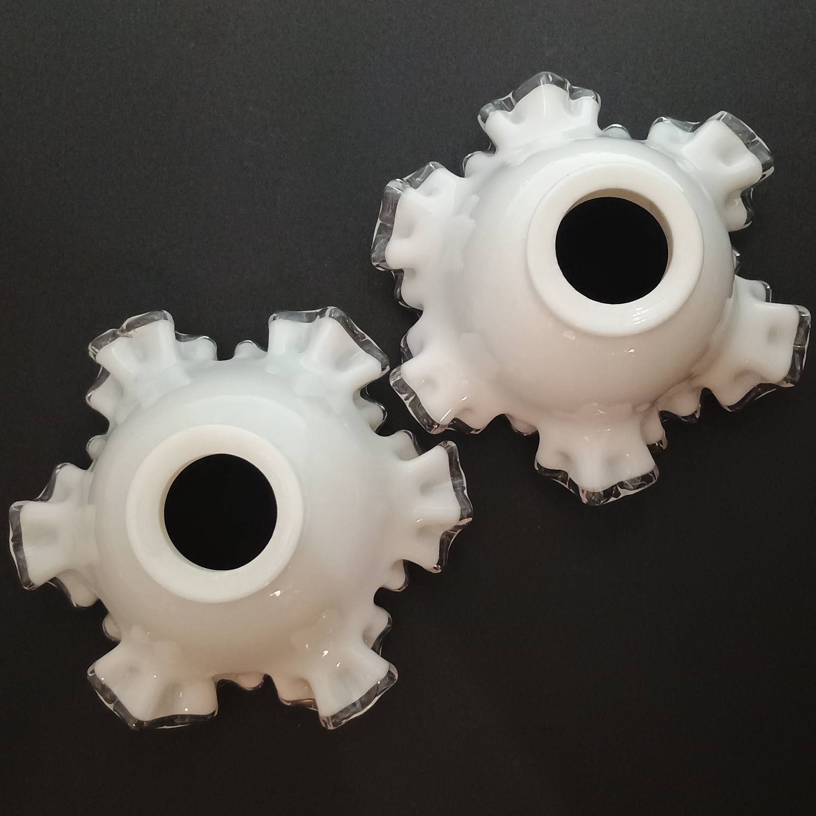 Two ruffled bell-shaped lampshades made of white glass with clear glass along the edges, photographed on a white background. One has a pinkish-purple tint.