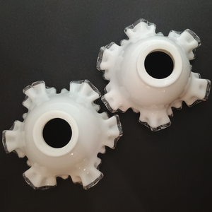 Two ruffled glass lamp shades made of white milk glass with clear glass along the edges, photographed on a dark grey background. The fitters thicker and shinier than usual.