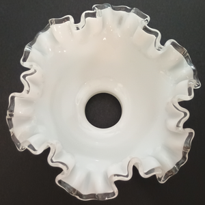 The interior of a ruffled milk glass lamp shade with clear glass along the edges, photographed on a dark grey background.