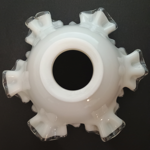 The base of a ruffled milk glass lamp shade with clear glass along the edges, photographed on a dark grey background. The fitter is unusually thick.