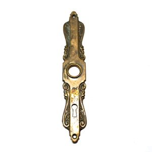 A brass Art Nouveau escutcheon, with intricate scrolling details and a keyhole near the bottom