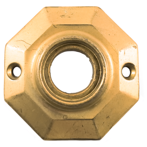 An octagonal brass rosette, with a hole in the middle for a doorknob and two screw holes oriented horizontally. The surface is somewhat scratched.