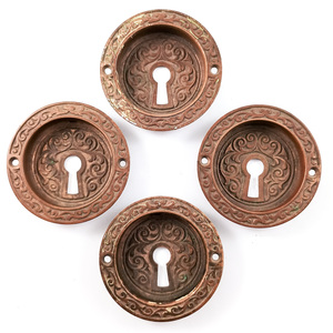Four round bronze door pills made of inset centers with rims, arranged in a diamond shape. Each one is decorated with swirling floral designs, and has a keyhole in the center and two screw holes in the rim.