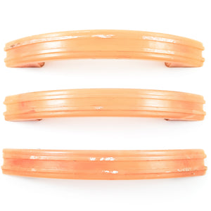 Three light orange drawer handles. Each one has two thin, raised stripes running the length of the handle, and they all have varying amounts of white paint on them.