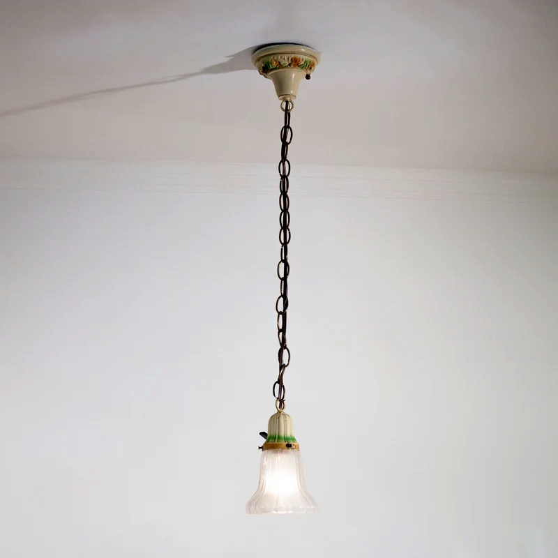 A vintage hanging pendant light with a cream-colored canopy and setting, both of which have hand-painted accents, and a glass tulip shade