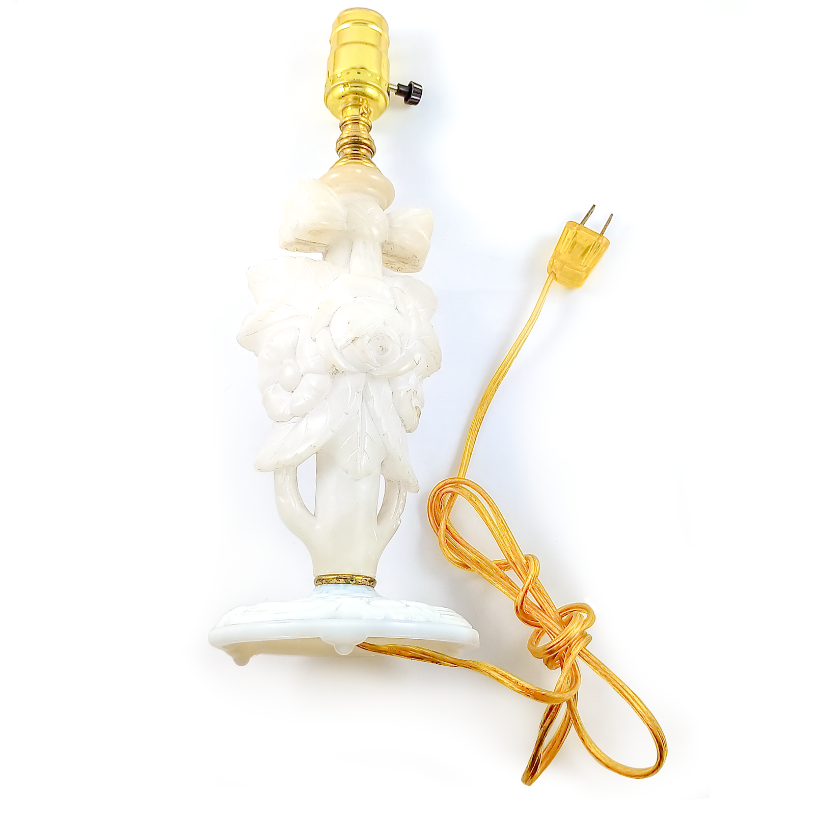 A table lamp made of carved alabaster with a glass base, a yellow corded plug, and a brass socket. The alabaster carving is in the shape of a rose with a bow above it.