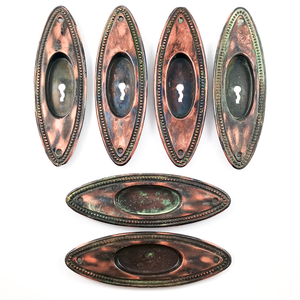 Six oval pocket door pulls with copper-and-black japanned finishes and beaded trim. Four have keyholes, two do not. There are varying amounts of verdigris and patina on each door pull.